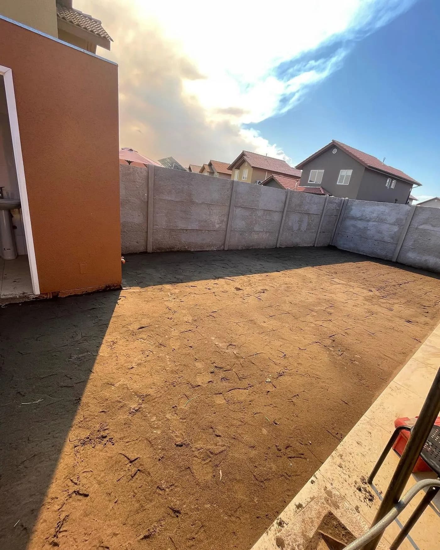 Patio de tierra sin intervenir, delimitado por un muro de hormigón, antes de comenzar la obra