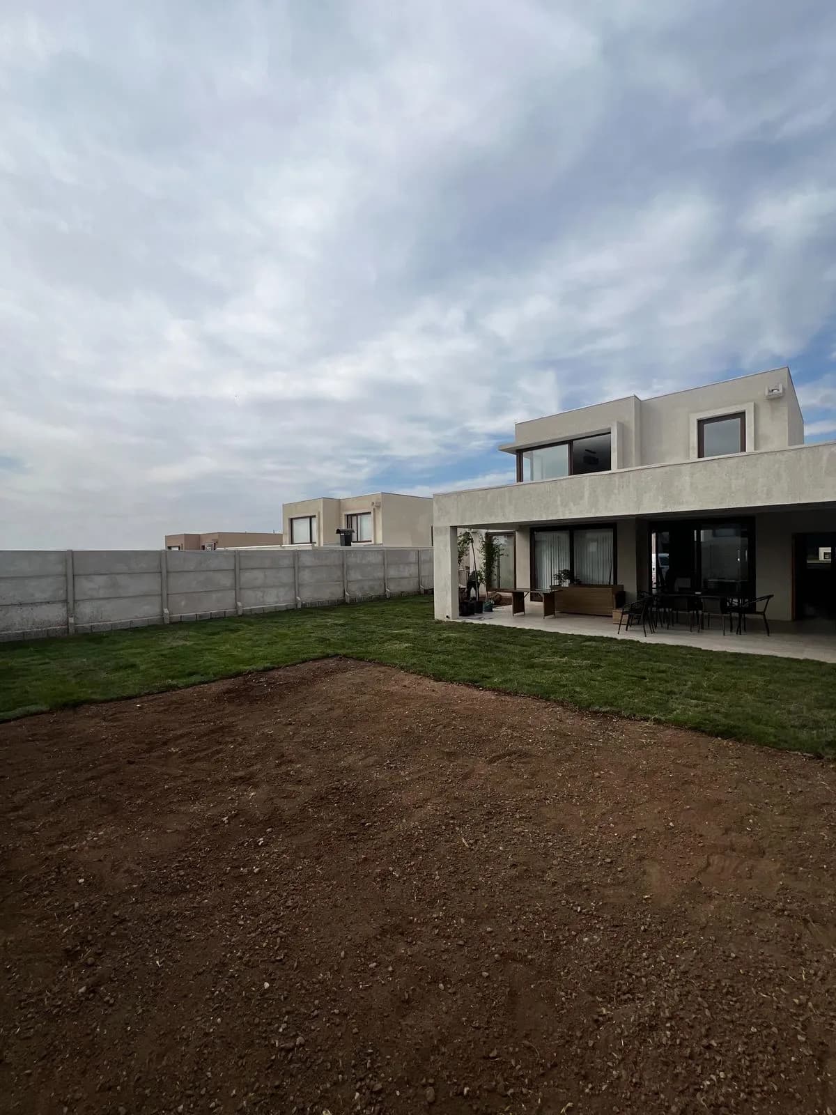 Patio de una casa con la mitad del terreno ya cubierto de pasto y la otra mitad de tierra nivelada, lista para instalar
