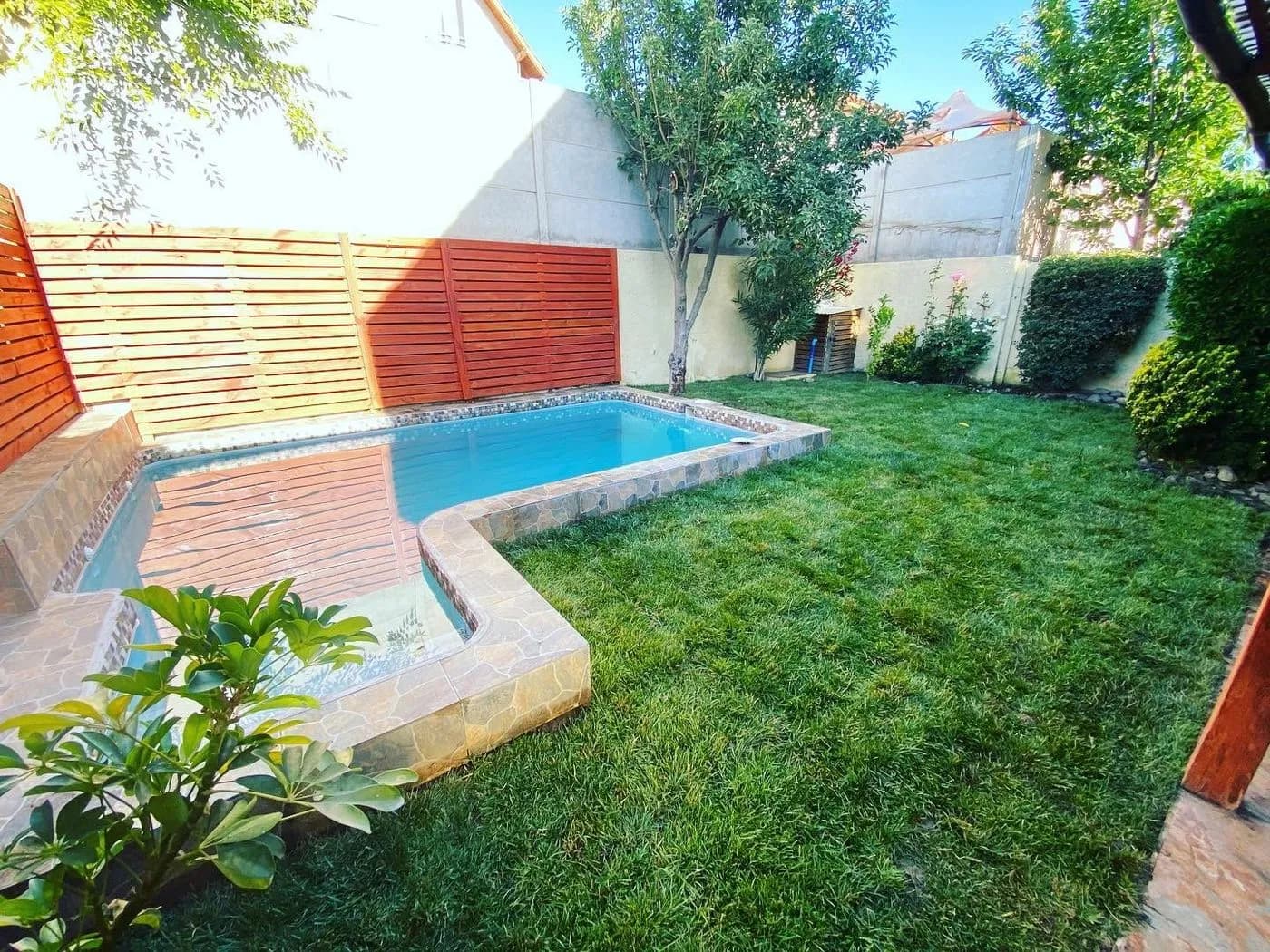 Jardín terminado con pasto natural instalado alrededor de una piscina, con borde de piedra y cierre de madera